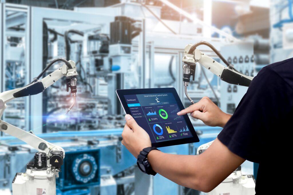 Ein Techniker nutzt ein Tablet zur Überwachung und Steuerung von industriellen Robotern in einer Produktionshalle.