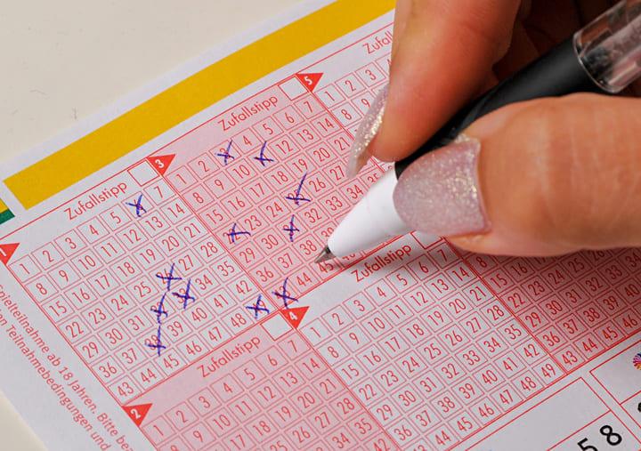 Hand mit einem Kugelschreiber kreuzt Zahlen auf einem Eurojackpot-Lottoschein an, effektive Tipps und Tricks, um Ihre Gewinnchancen zu steigern.
